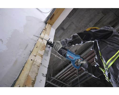 Ein Handwerker schneidet mit einer Bosch Professional Säbelsäge einen Holzbalken an einer Wand auf einer Baustelle.