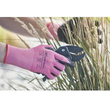 Eine Person schneidet Gras mit einer Gartenschere und trägt dabei Gartenhandschuhe.