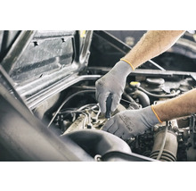 Ein Mechaniker, der mit Schutzhandschuhen an einem Automotor arbeitet.