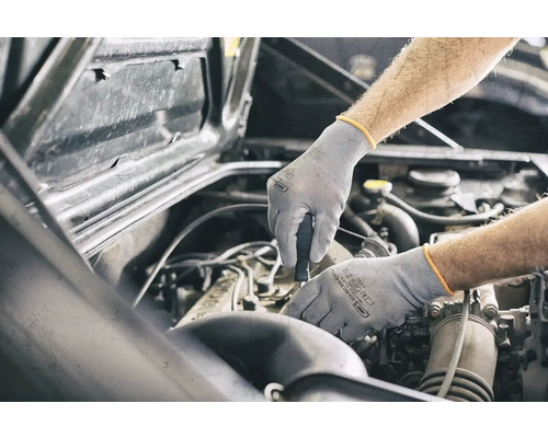 Ein Mechaniker, der mit Schutzhandschuhen an einem Automotor arbeitet.