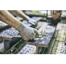 Eine Person misst ein Metallstück mit einem digitalen Messschieber auf einem Träger.