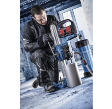 Handwerker bedient ein Bosch Akku-Diamantkernbohrgerät mit Bohrständer auf einem Betonboden in einer Baustellenumgebung.