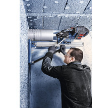 Handwerker mit Schutzausrüstung bedient eine Kernbohrmaschine mit Bohrständer an einer Betonwand.