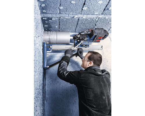 Handwerker mit Schutzausrüstung bedient eine Kernbohrmaschine mit Bohrständer an einer Betonwand.