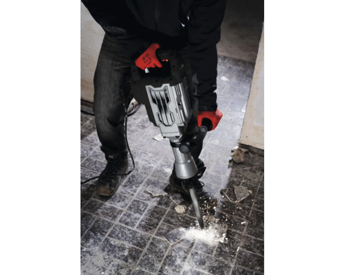 Ein Mann mit Arbeitshandschuhen benutzt einen Abbruchhammer, um Fliesen zu entfernen.