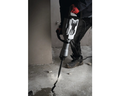 Ein Mann benutzt einen Abbruchhammer, um einen Riss in einen Betonboden zu schlagen.