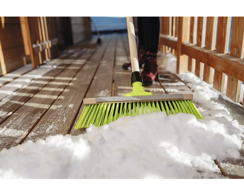 Schneeräumen mit einem Besen auf einer Holzterrasse