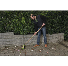 Eine Person kehrt Blätter mit einem Straßenbesen.