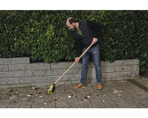 Eine Person kehrt Blätter mit einem Straßenbesen.