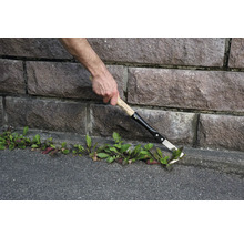 Gartenarbeiter entfernt Unkraut mit einem Fugenkratzer an einer Steinmauer