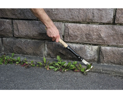 Gartenarbeiter entfernt Unkraut mit einem Fugenkratzer an einer Steinmauer