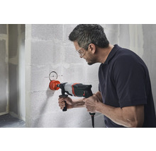 Mann bohrt mit einer Kernbohrmaschine ein Loch in eine Betonwand.