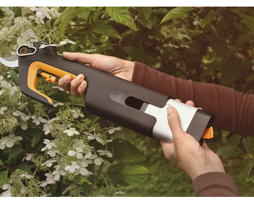 Gartenarbeit mit einer Akku-Gartenschere in der Hand vor einem blühenden Busch