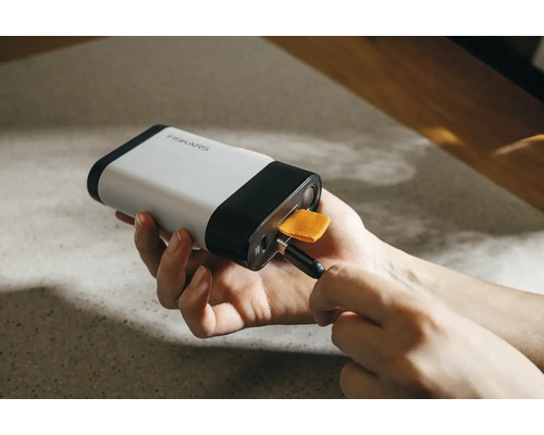 Fiskars Logo, eine Person schliesst ein USB-Kabel an eine Powerbank an.