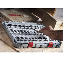 Bosch Fräser Set für Oberfräsen in einer Kunststoffbox auf einem Holztisch mit Hand, die einen Fräser hält.