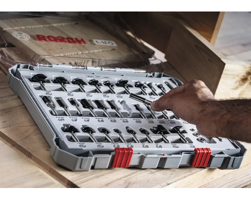 Bosch Fräser Set für Oberfräsen in einer Kunststoffbox auf einem Holztisch mit Hand, die einen Fräser hält.