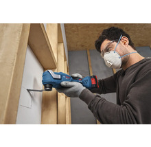 Person mit Schutzausrüstung schneidet mit einem Bosch Akkumulator-Multitool eine Öffnung in eine Wandbauplatte zwischen Holzständerwerk.