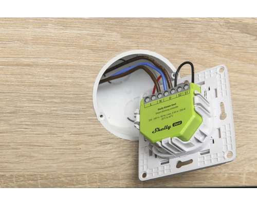 Shelly Dimmer Gen4 smarter Dimm-Controller bei der Installation in einer Unterputzdose mit angeschlossener Verkabelung an einem Lichtschalterrahmen.