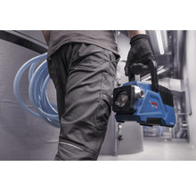 Person in Arbeitskleidung trägt eine batteriebetriebene blaue Bosch Wasserpumpe und einen aufgerollten Schlauch in einem hellen Arbeitsbereich.