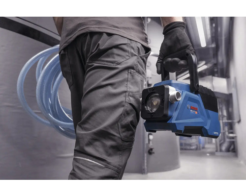 Person in Arbeitskleidung trägt eine batteriebetriebene blaue Bosch Wasserpumpe und einen aufgerollten Schlauch in einem hellen Arbeitsbereich.