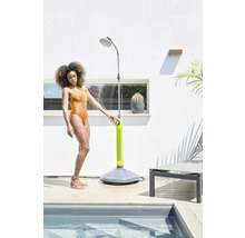 Frau benutzt eine Gartenbrause neben einem Schwimmbecken auf einer Terrasse.