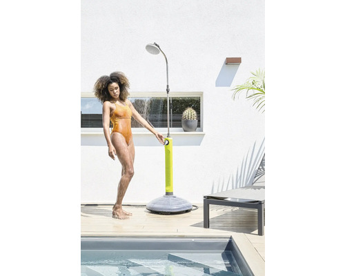 Frau benutzt eine Gartenbrause neben einem Schwimmbecken auf einer Terrasse.