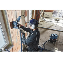 Handwerker nutzt eine Mauernutfräse an einer Ziegelwand. Staubabsaugung ist angeschlossen.