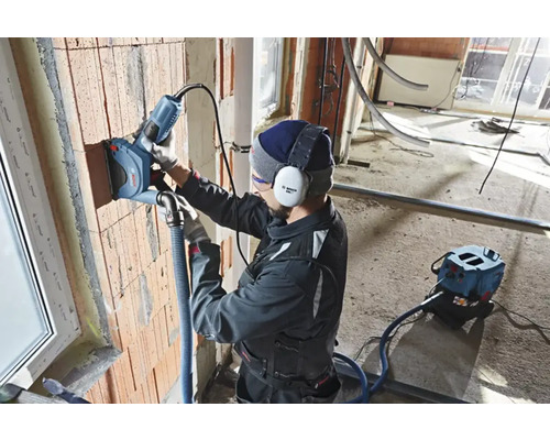 Handwerker nutzt eine Mauernutfräse an einer Ziegelwand. Staubabsaugung ist angeschlossen.