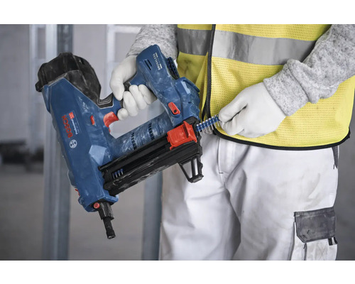 Eine Person befüllt einen blauen Bolzensetzer mit Bolzen.