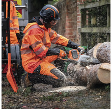Ein Mann in Schutzkleidung sägt Holz mit einer Kettensäge.