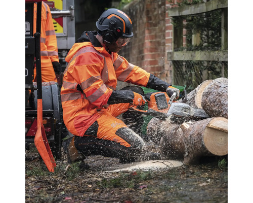 Ein Mann in Schutzkleidung sägt Holz mit einer Kettensäge.