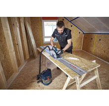 Handwerker schneidet OSB-Platte mit Bosch Handkreissäge auf Führungsschiene mit angeschlossenem Staubsauger beim Dachausbau.