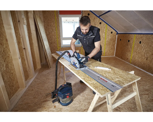 Handwerker schneidet OSB-Platte mit Bosch Handkreissäge auf Führungsschiene mit angeschlossenem Staubsauger beim Dachausbau.