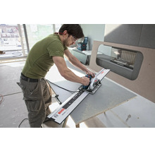 Ein Mann schneidet mit einer Handkreissäge und Führungsschiene ein Werkstück.