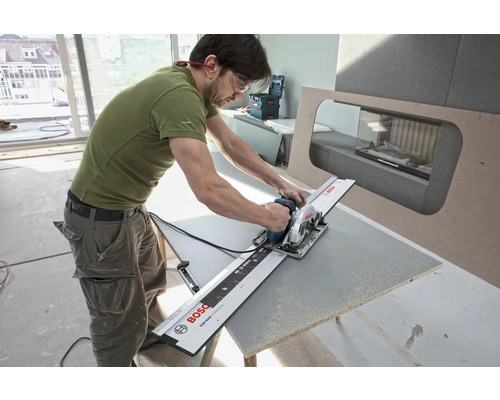 Ein Mann schneidet mit einer Handkreissäge und Führungsschiene ein Werkstück.