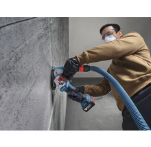 Eine Person nutzt eine Bosch 18 Volt Akku-Mauernutfräse mit Staubabsaugung an einer Betonwand entlang einer grünen Lasermarkierung.