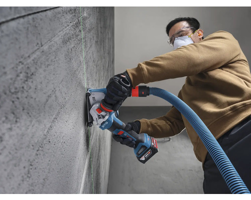 Eine Person nutzt eine Bosch 18 Volt Akku-Mauernutfräse mit Staubabsaugung an einer Betonwand entlang einer grünen Lasermarkierung.