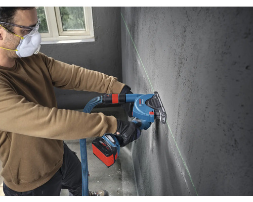 Handwerker verwendet eine akkubetriebene Mauernutfräse mit Staubabsaugung und Laserführung an einer Betonwand. Bosch Professional Logo.