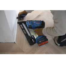 Bosch Akku-Nagler Professional GNH 18V-64 MD bei der Montage einer Fußleiste auf einem hellen Holzboden in Fischgrätoptik.