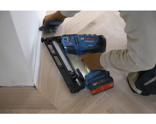 Bosch Akku-Nagler Professional GNH 18V-64 MD bei der Montage einer Fußleiste auf einem hellen Holzboden in Fischgrätoptik.