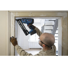 Handwerker befestigt eine Holzleiste an einem Türrahmen mit einem Bosch Akku-Nagler in einem hellen Innenraum.