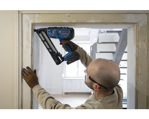 Handwerker befestigt eine Holzleiste an einem Türrahmen mit einem Bosch Akku-Nagler in einem hellen Innenraum.