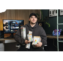 Mann im grauen Hoodie präsentiert Osram Smart Plus Beleuchtungsprodukte in einem modernen Büro mit Holzpaneelwand.