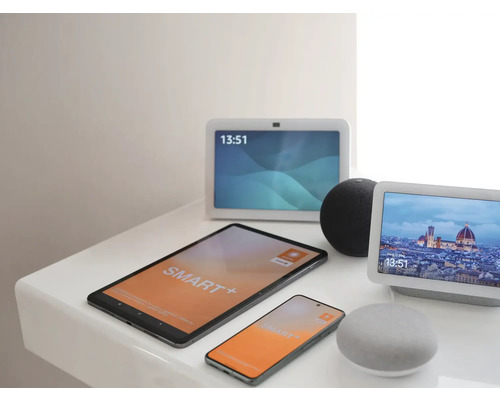 Verschiedene Smart Home Geräte wie Tablet, Smartphone, zwei Smart Displays und zwei Smart Speaker auf einer Ablage.