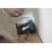Person befestigt eine weiße Sockelleiste mit einem Bosch Akku-Nagler auf einem hellen Holzfußboden.