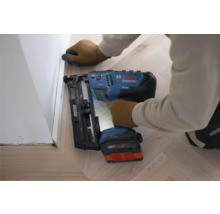 Bosch Akku-Nagler befestigt eine weiße Sockelleiste auf einem hellen Holzboden.