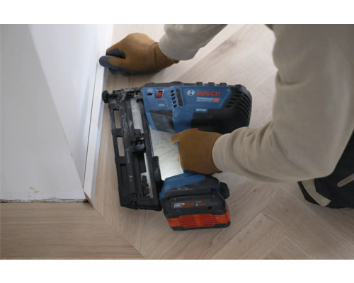 Bosch Akku-Nagler befestigt eine weiße Sockelleiste auf einem hellen Holzboden.