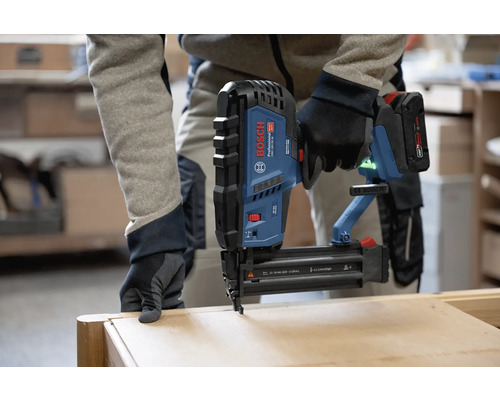 Eine Person benutzt einen Bosch Professional Akku-Nagler auf einem Werkstück aus Holz.