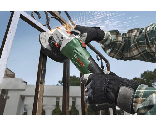 Person bearbeitet einen Metallzaun mit einem Bosch Akkumulator Winkelschleifer PWS 18V-70 im Freien mit Funkenflug.