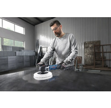 Ein Handwerker mit Schutzbrille poliert eine dunkle Metallfläche in einer hellen, geräumigen Werkstatt mit einer Bosch Poliermaschine.